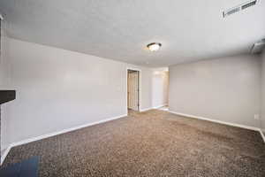 Carpeted basement living room featuring baseboards and a textured ceiling