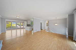 Unfurnished living room with ornamental molding, light wood-style floors, and baseboards