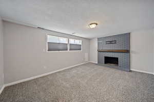 Unfurnished basement living room featuring a fireplace, a textured ceiling, carpet floors, and baseboards