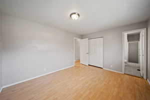 Unfurnished bedroom featuring light wood-style floors, baseboards, a closet, and connected bathroom