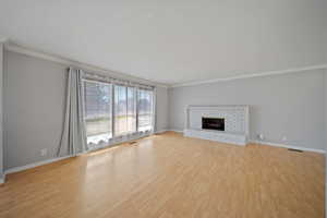 Unfurnished living room featuring crown molding, light wood-style floors, baseboards, and a brick fireplace