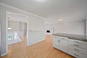 Kitchen featuring ornamental molding, light wood-style flooring, white cabinets, baseboards, and a brick fireplace