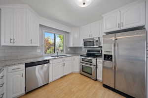 Kitchen with stainless steel appliances, a sink, light wood-style flooring, tasteful backsplash, and white cabinetry