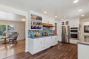 Remodeled  kitchen with stainless steel appliances with stainless steel finishes, white Shaker-style cabinetry, tasteful marble tile backsplash, under cabinet range hood, and recessed lighting
