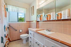 Full bBathroom with toilet, vanity, original tile walls and counter