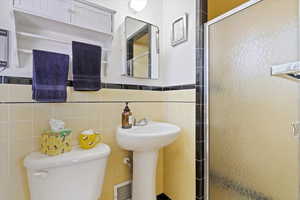 Three-quarter bathroom with a stall shower, toilet, a pedestal sink, and original 1956 tile walls