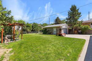 View of yard with a hand-built pergola with grape vines, a garage, and concrete driveway