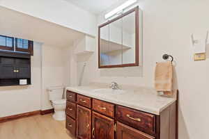 Half bathroom featuring wood finished floors, toilet, vanity, and baseboards