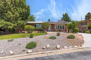 Ranch-style home with brick siding, roof mounted solar panels, covered porch, driveway, and a front yard
