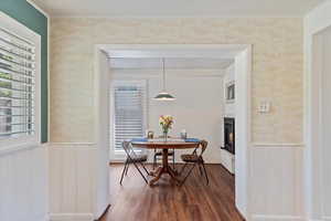 Dining room with dark wood finished floors, healthy amount of natural light, radiant heat style fireplace, a wainscoted wall, and ornamental molding