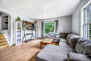 Living room featuring a baseboard heating unit, wood finished floors, plenty of natural light, and stairs