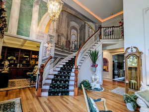 Staircase with a towering ceiling, wood finished floors, a chandelier, and ornamental molding