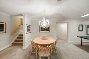 Dining room with carpet, a chandelier, stairs, and ornamental molding