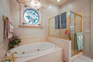 Full bathroom with a shower stall, a tub with jets, a chandelier, and crown molding