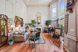 Living area featuring a high ceiling, wood finished floors, a glass covered fireplace, and ornamental molding
