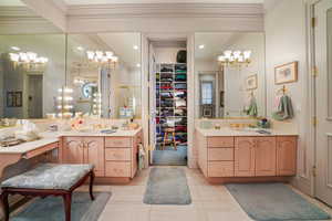 Bathroom with a chandelier, crown molding, a shower stall, two vanities, and tile patterned floors