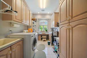 Washroom with cabinet space, separate washer and dryer, crown molding, light tile patterned floors, and a desk