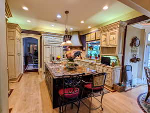 Kitchen featuring custom range hood, ornamental molding, light wood-style floors, cream cabinets, and a kitchen island