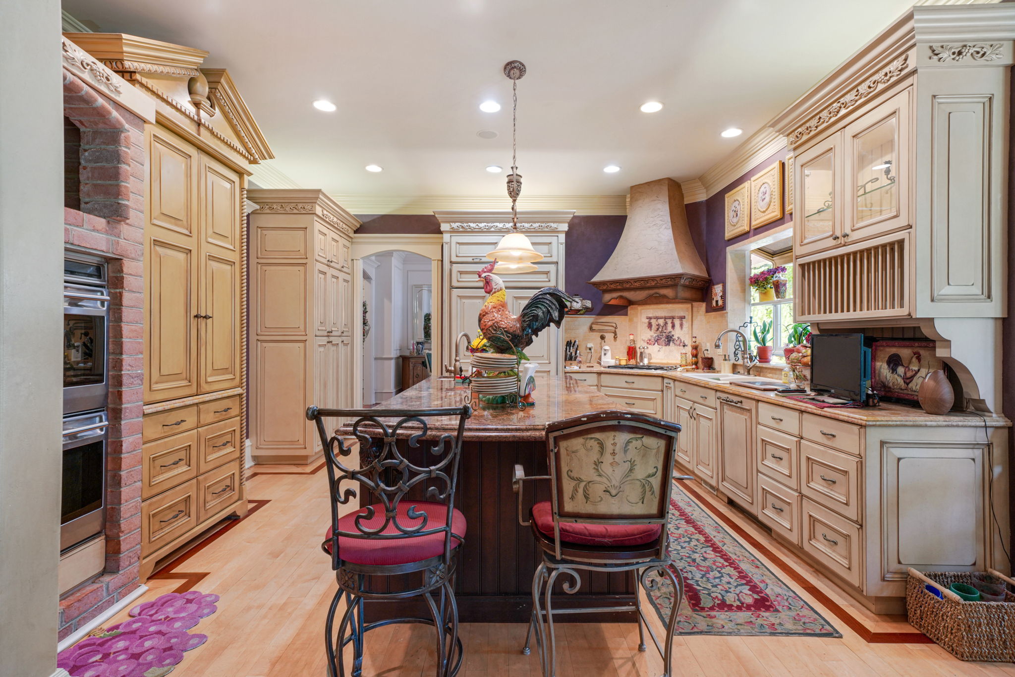 Kitchen with cream cabinetry, light wood-type flooring, crown molding, pendant lighting, and premium range hood