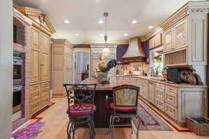 Kitchen with cream cabinetry, light wood-type flooring, crown molding, pendant lighting, and premium range hood