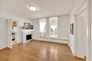 Unfurnished living room featuring radiator, light wood-style flooring, crown molding, a tiled fireplace, and baseboards