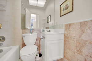 Bathroom with tile walls, toilet, vanity, a wainscoted wall, and tile patterned flooring