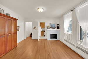 Unfurnished living room with light wood-style flooring, a baseboard heating unit, a tile fireplace, crown molding, and baseboards