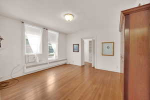 Unfurnished room with a baseboard heating unit, light wood-style floors, and baseboards