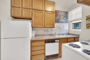 Kitchen with white appliances, a sink, backsplash, and light brown cabinets