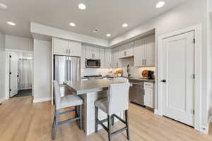 Kitchen with appliances with stainless steel finishes, a sink, a kitchen breakfast bar, light wood-type flooring, and recessed lighting