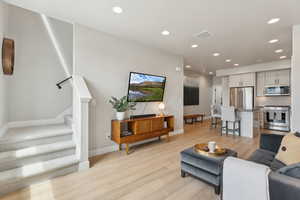 Living area with light wood finished floors, recessed lighting, stairway, and baseboards