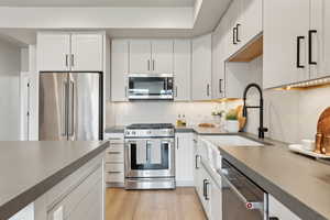 Kitchen featuring stainless steel appliances, a sink, dark countertops, white cabinets, and decorative backsplash