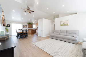 Living room featuring lofted ceiling, ceiling fan, light wood-style flooring, baseboards, and recessed lighting