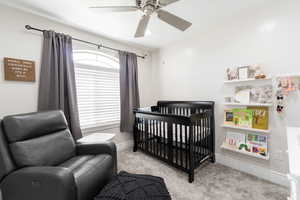 Bedroom featuring a crib, carpet, ceiling fan, and baseboards