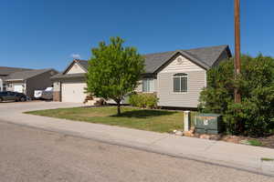 Ranch-style home featuring an attached garage, concrete driveway, a front lawn, and roof with shingles
