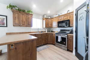 Kitchen featuring black microwave, stainless steel gas stove, a sink, a peninsula, and light wood-style floors
