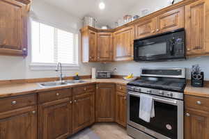 Kitchen with black microwave, stainless steel gas range, a sink, light countertops, and brown cabinets