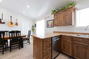 Kitchen with a sink, dishwasher, vaulted ceiling, light wood-style floors, and a peninsula