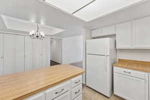 Kitchen featuring freestanding refrigerator, white cabinets, a chandelier, and wooden counters