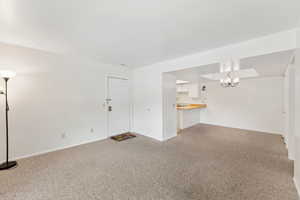 Unfurnished living room featuring light colored carpet, a chandelier, and baseboards
