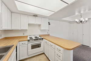 Kitchen featuring electric stove, a peninsula, white cabinets, and a sink