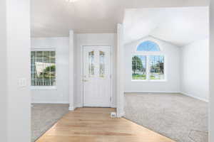 Entrance foyer with light carpet, vaulted ceiling, baseboards, and light wood-type flooring