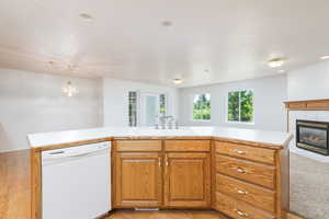 Kitchen island with dishwasher, a sink, light countertops, a tile fireplace, and light wood-style floors