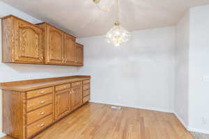 Kitchen with brown cabinetry, light wood-type flooring, a chandelier, baseboards, and decorative light fixtures