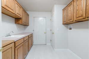 Washroom/Laundry Room with new flooring with cabinet space, washer/dryer hookups, baseboards, a textured ceiling, and light floors