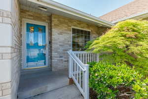 View of exterior entry featuring brick siding, a porch, and a shingled roof
