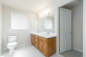 Bathroom featuring toilet, baseboards, and double vanity