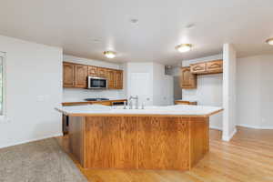Kitchen featuring stainless steel microwave, a sink, gas cooktop, light countertops, and brown cabinetry