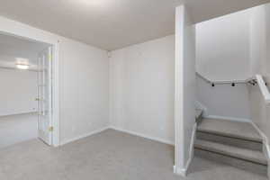 Stairway featuring carpet, a textured ceiling, and baseboards