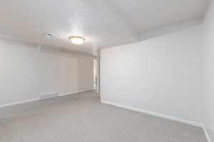 Unfurnished room featuring light carpet, baseboards, and a textured ceiling